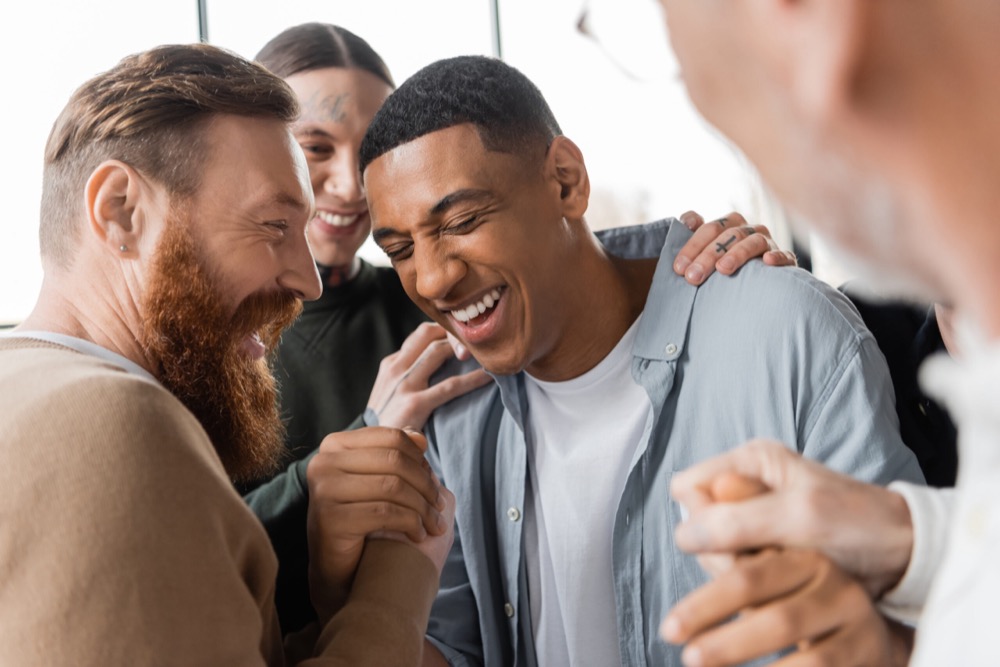 Positive people hugging african american man during alcoholics meeting and therapy in rehab center,stock image